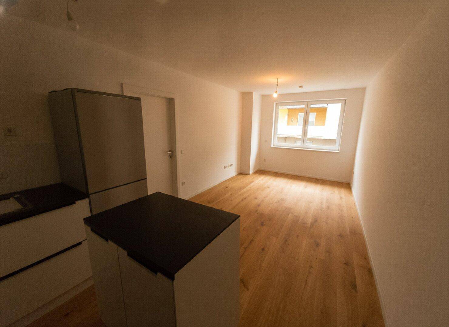 Heller Wohnbereich mit Holzboden, Fenster und vorbereiteter Küchenzeile.