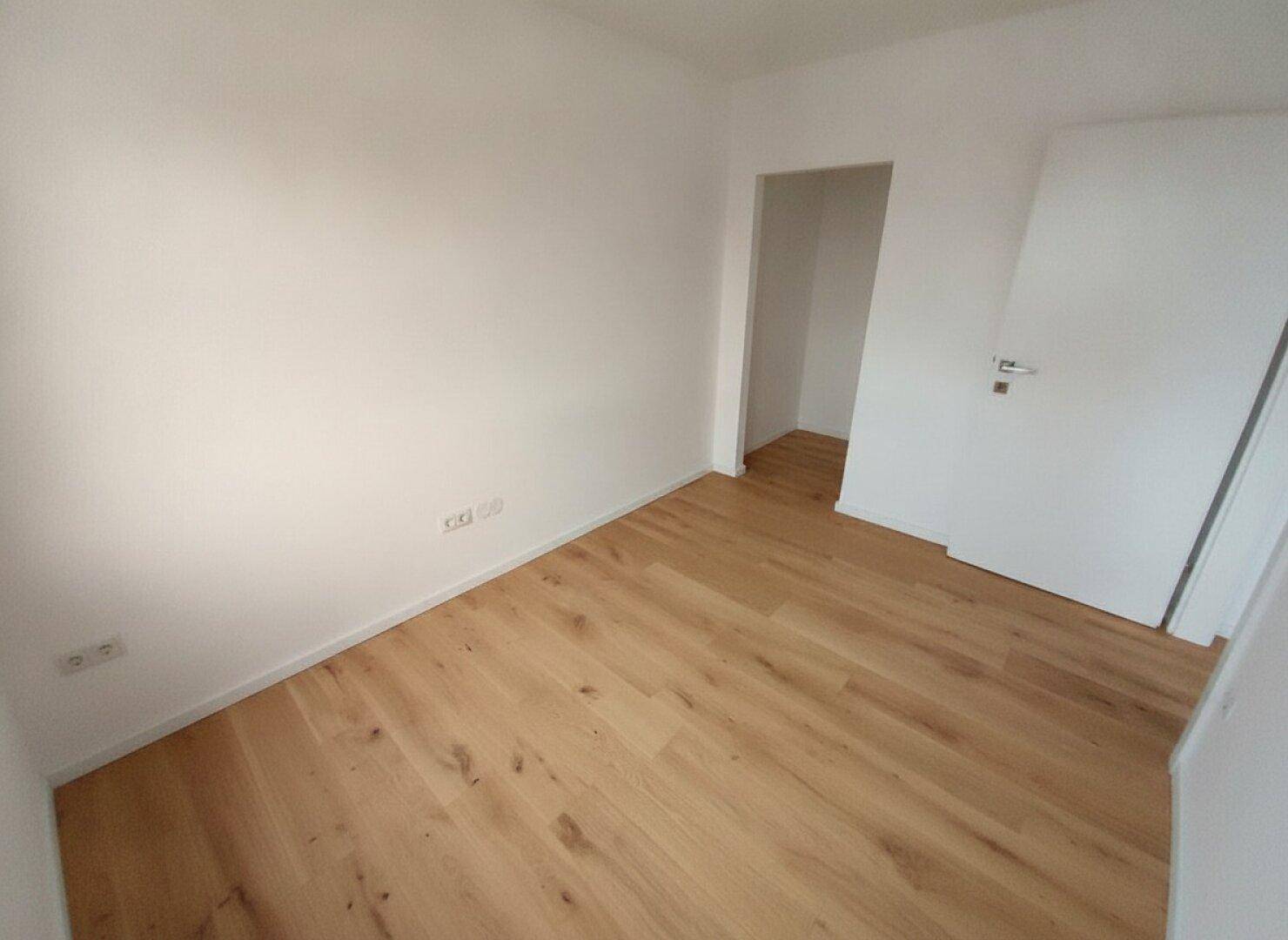 Helles, leeres Zimmer mit Holzboden und weiß gestrichenen Wänden, bereit zur Einrichtung.