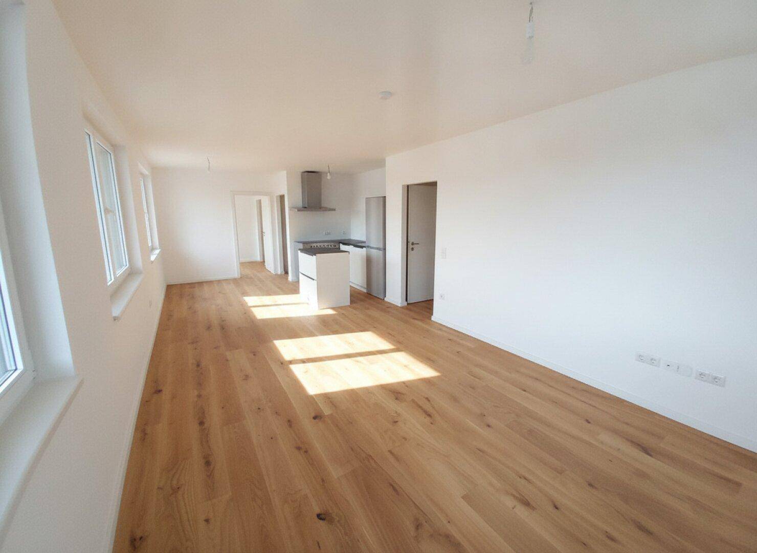 Lichtdurchfluteter offener Wohnbereich mit Holzboden und Küchenzeile, ideal für moderne Wohnkonzepte.