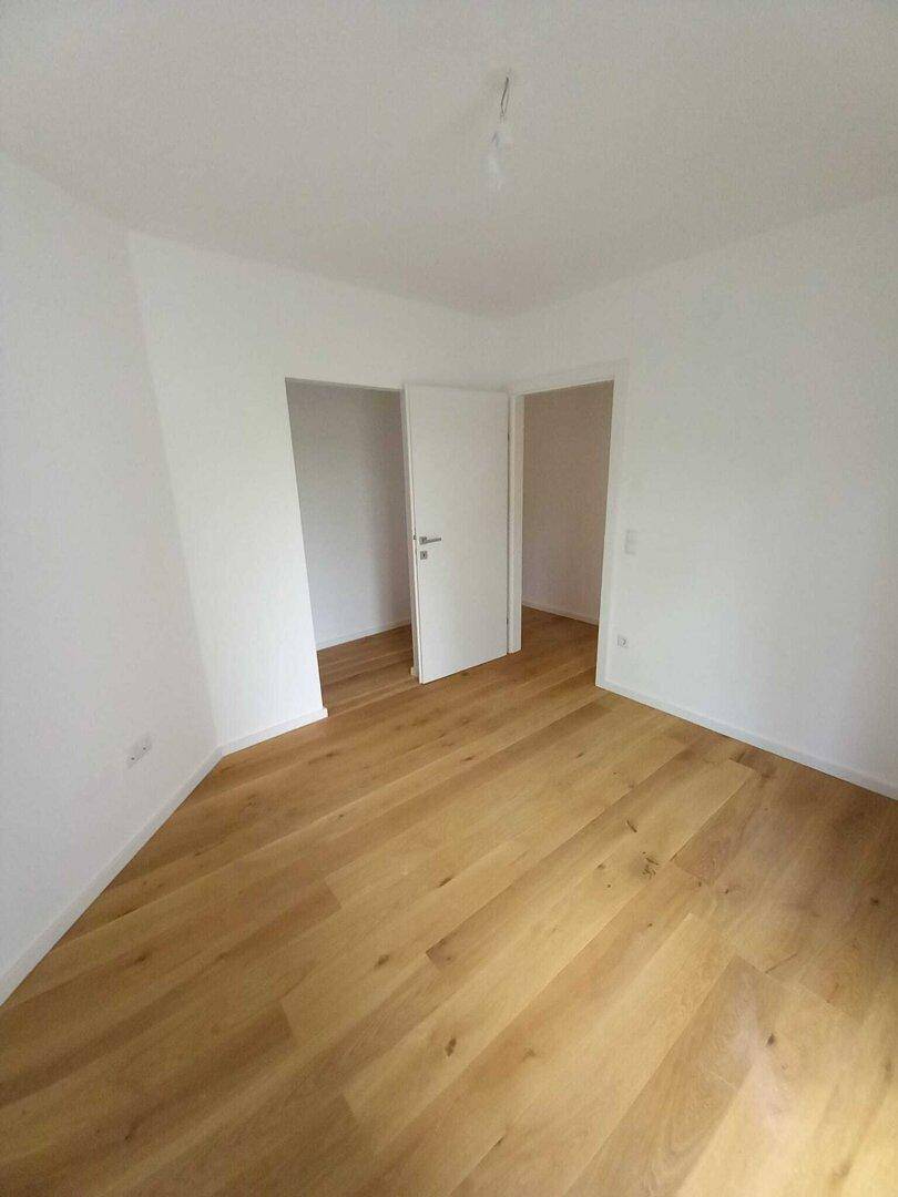 Heller Raum mit Holzparkett und zwei offenen Türrahmen, der zu weiteren Zimmern führt.