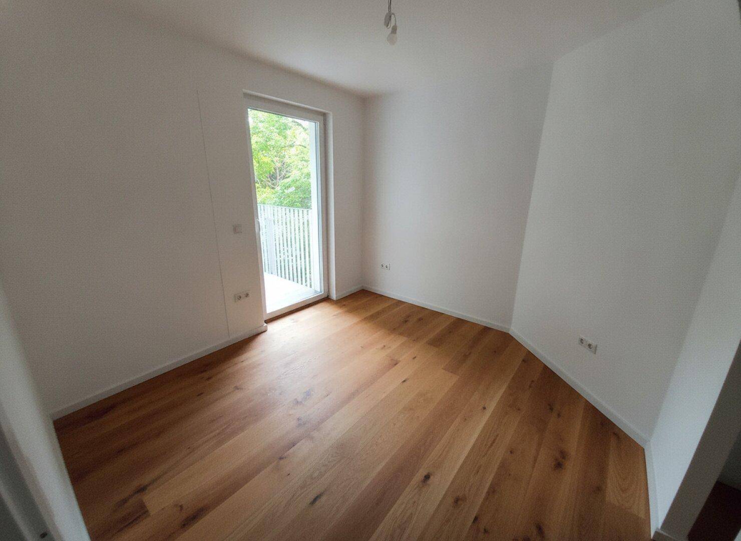 Kleinerer, heller Raum mit Holzparkett und Balkontür, ideal als Schlaf- oder Arbeitszimmer.