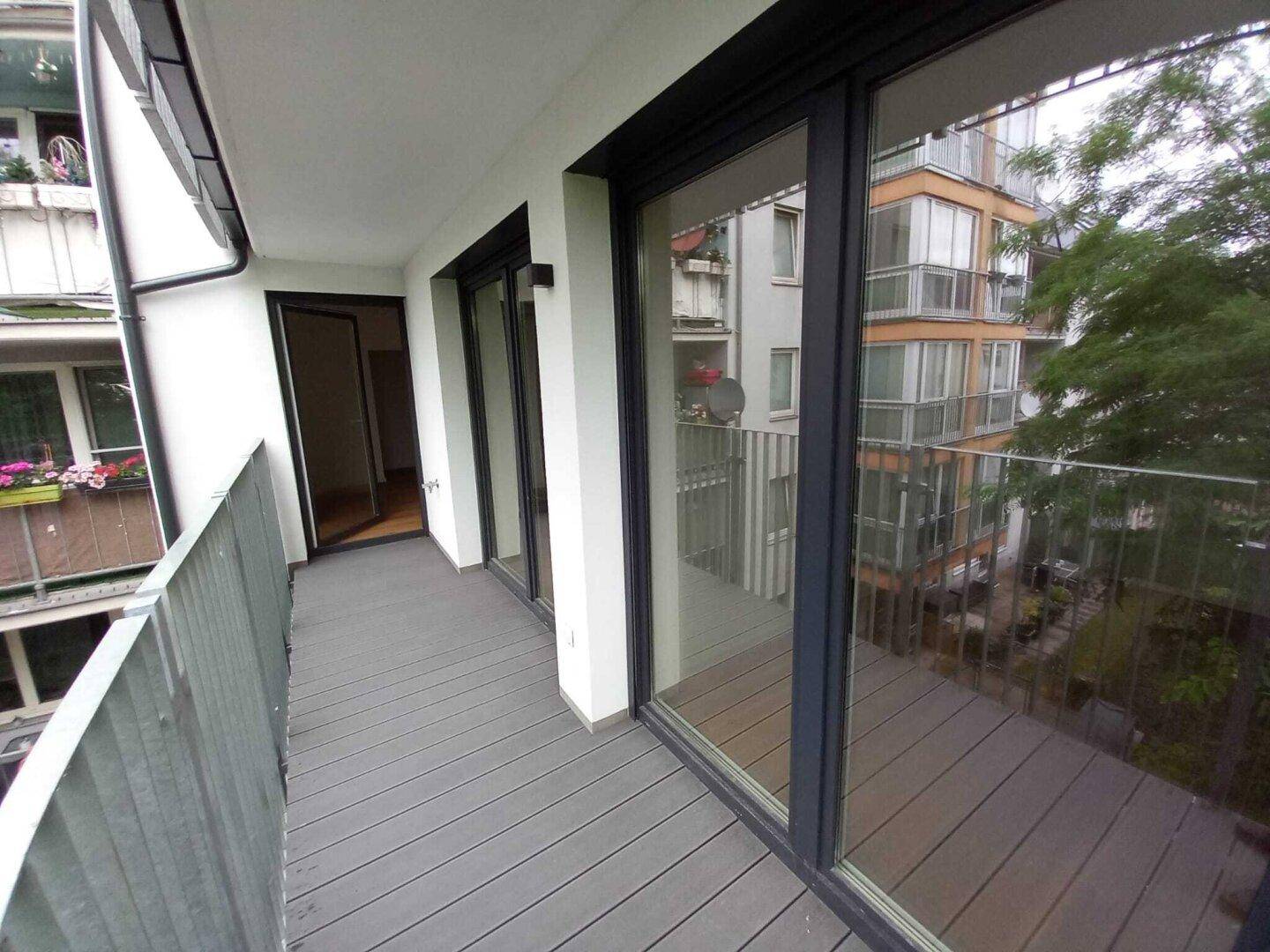 Geräumiger Balkon mit grauen Dielen, großen Schiebetüren und Blick auf die Umgebung.