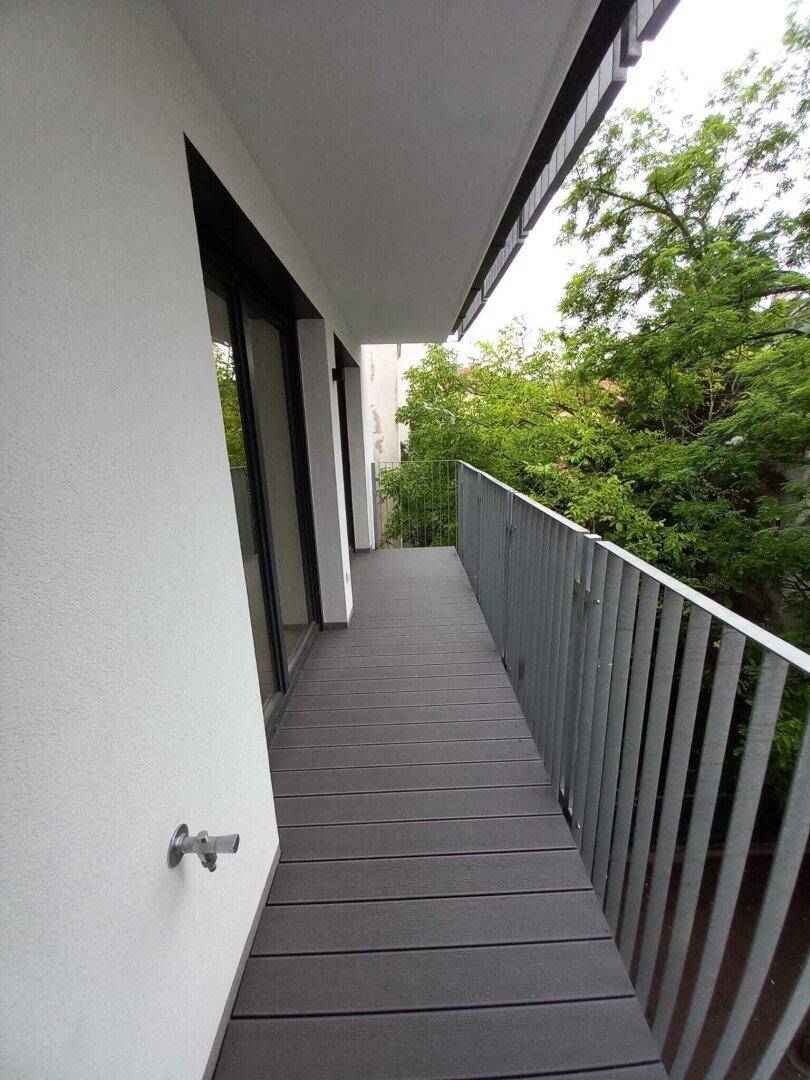 Langer, schmaler Balkon mit modernen grauen Dielen und Blick ins Grüne.