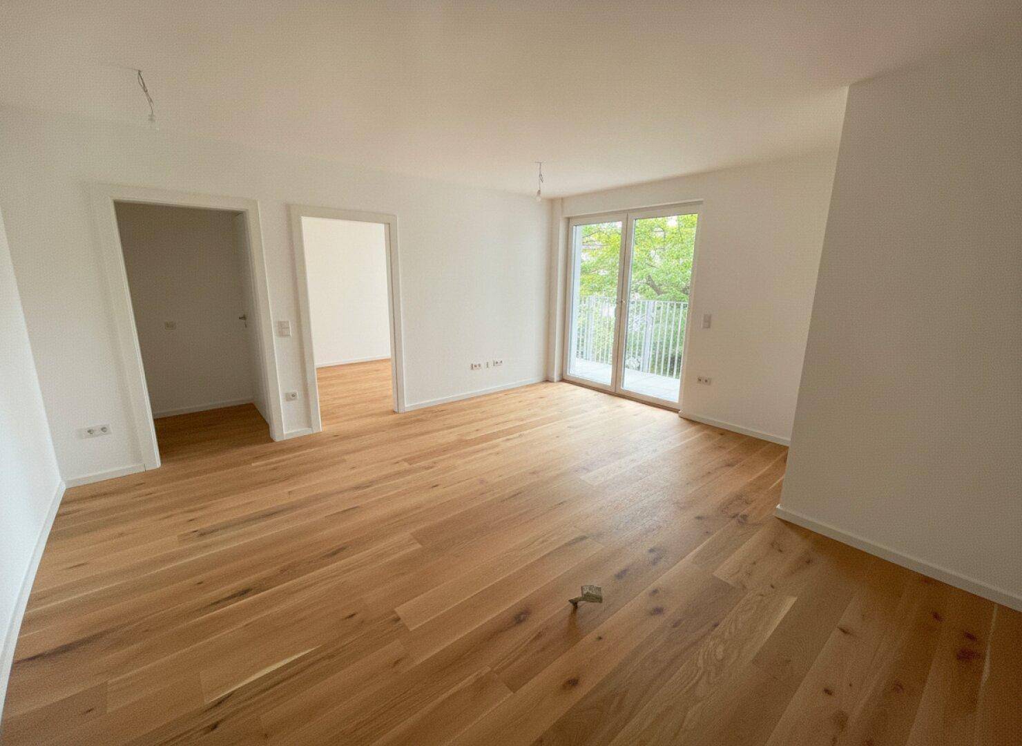 Geräumiger, heller Raum mit Holzparkett, zwei Türen und Balkonzugang.