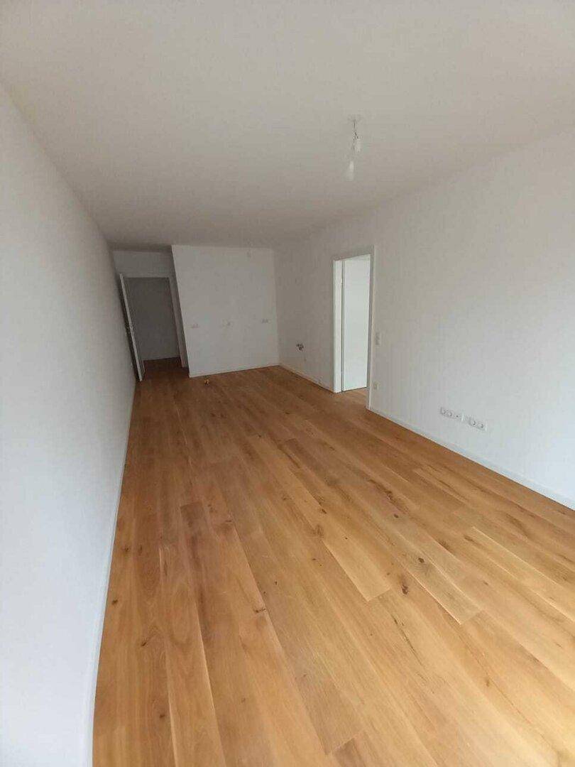 Langer, leerer Flur mit hellem Holzboden und mehreren Türöffnungen zu anderen Räumen.