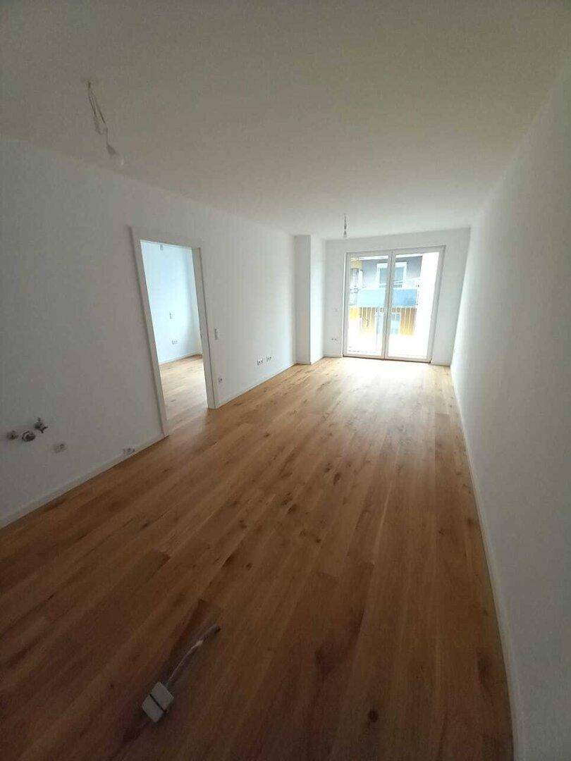Heller, leerer Raum mit Holzboden und Zugang zu einem Balkon oder einer Terrasse.