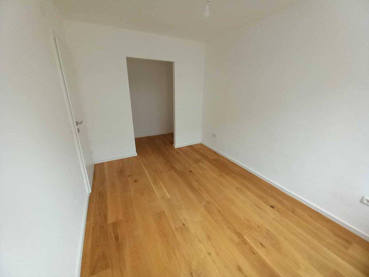 Leeres Zimmer mit Holzboden und weiß gestrichenen Wänden, bereit zur individuellen Gestaltung.
