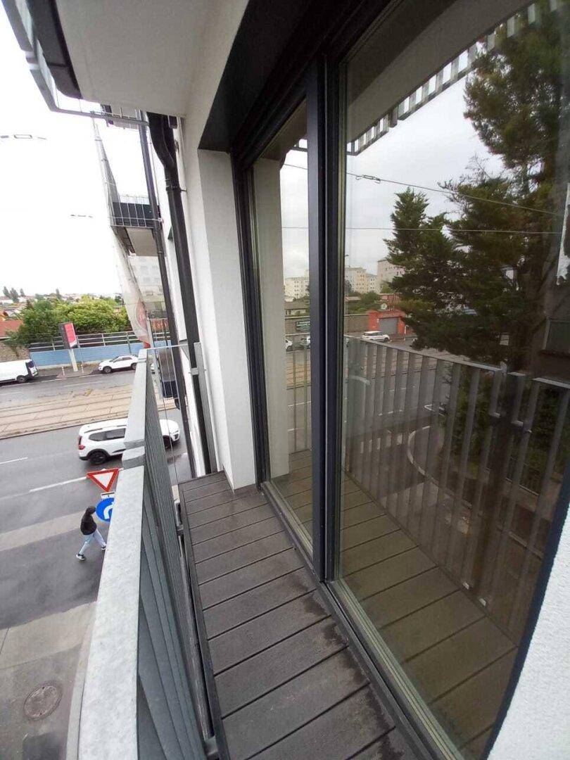 Schmaler Balkon mit dunklem Bodenbelag und Blick auf die darunterliegende Straße.