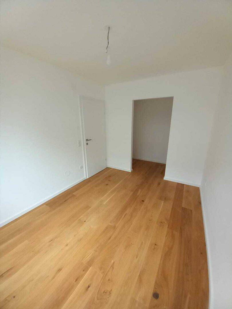 Helles, leeres Zimmer mit Holzboden und weiß gestrichenen Wänden, ideal als Schlafzimmer.