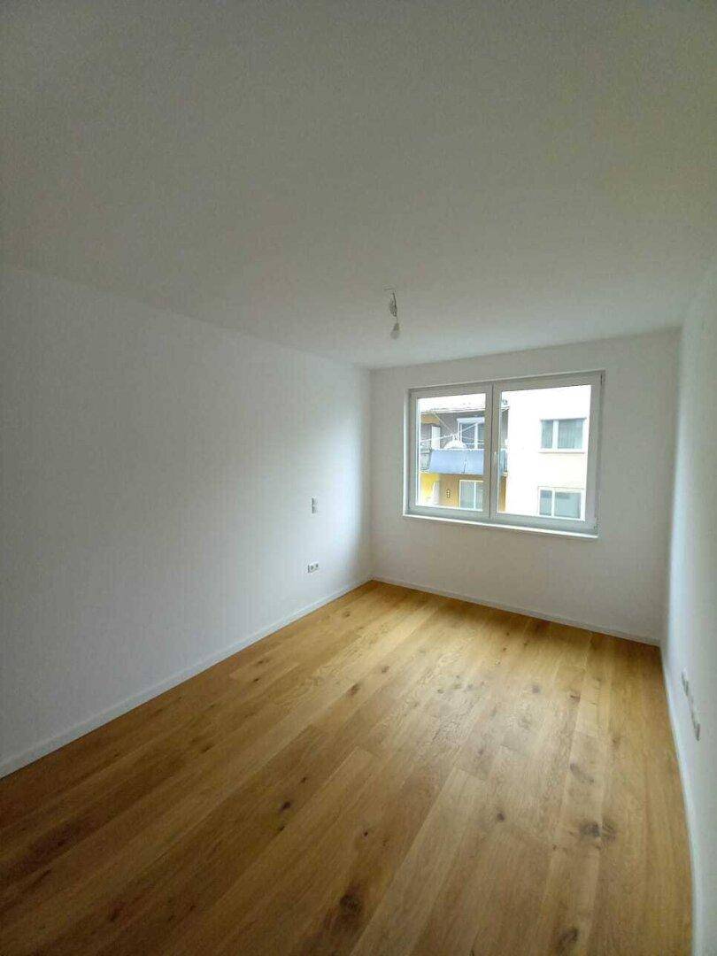 Helles Schlafzimmer mit Holzdielenboden und Blick auf die umliegenden Gebäude.