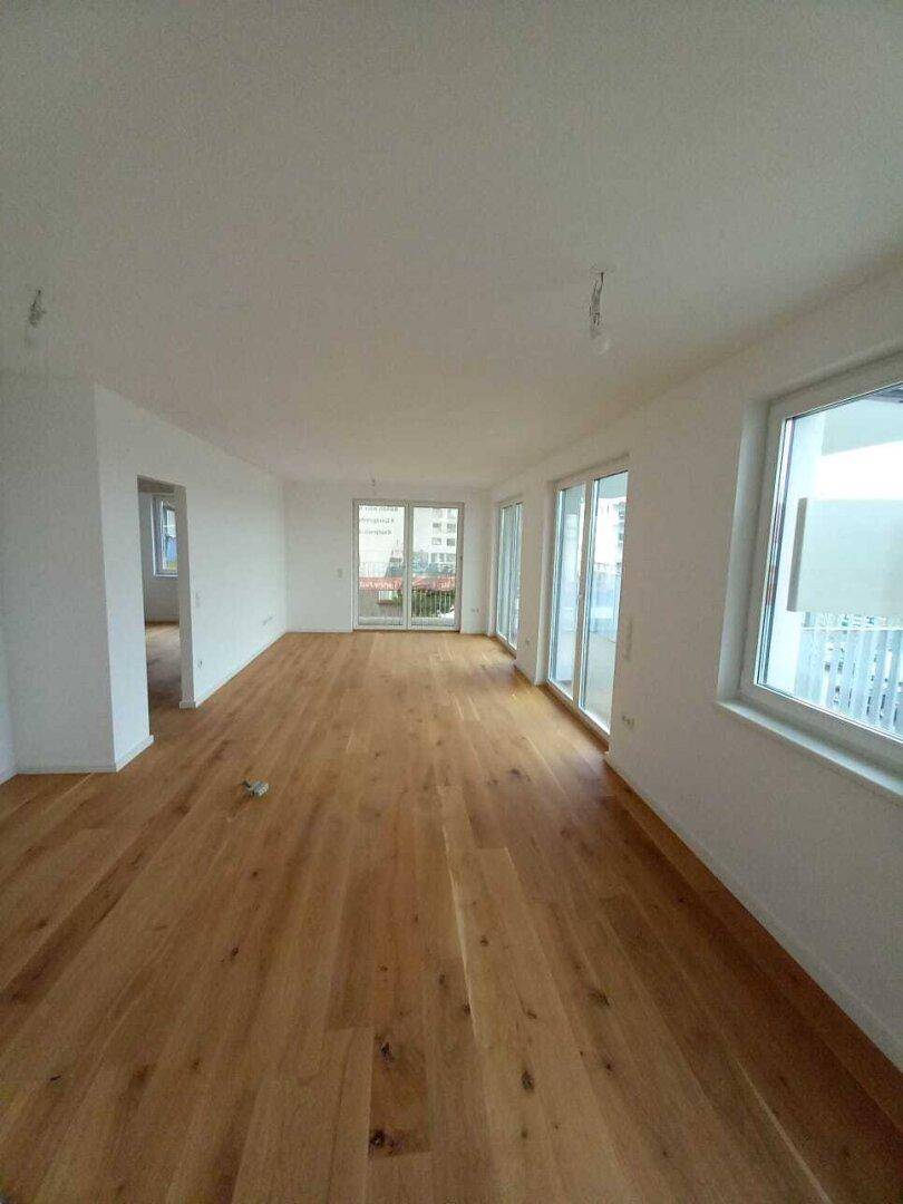 Geräumiger, unmöblierter Raum mit hellem Holzboden und viel Tageslicht durch große Fenster.