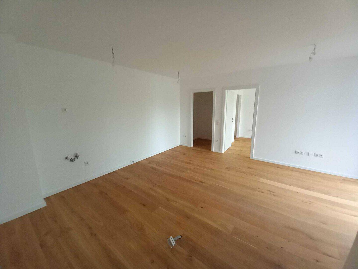 Leerer Wohnraum mit hellem Holzboden und weißen Wänden, bereit für individuelle Gestaltung.