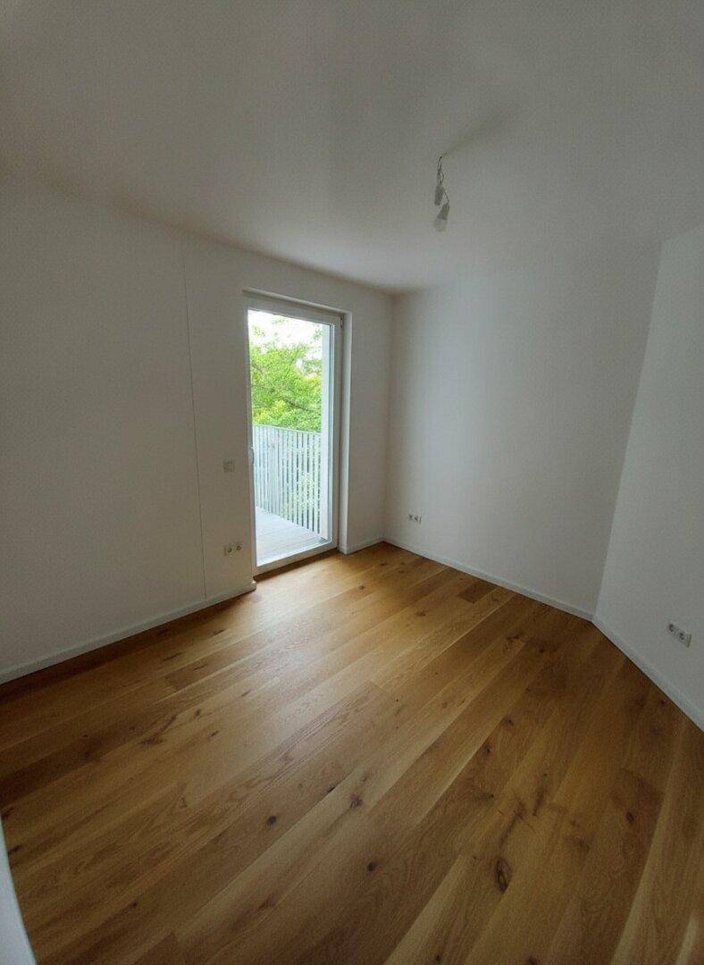 Helles, unmöbliertes Zimmer mit Holzboden und Balkonzugang, ideal als Schlaf- oder Arbeitszimmer.