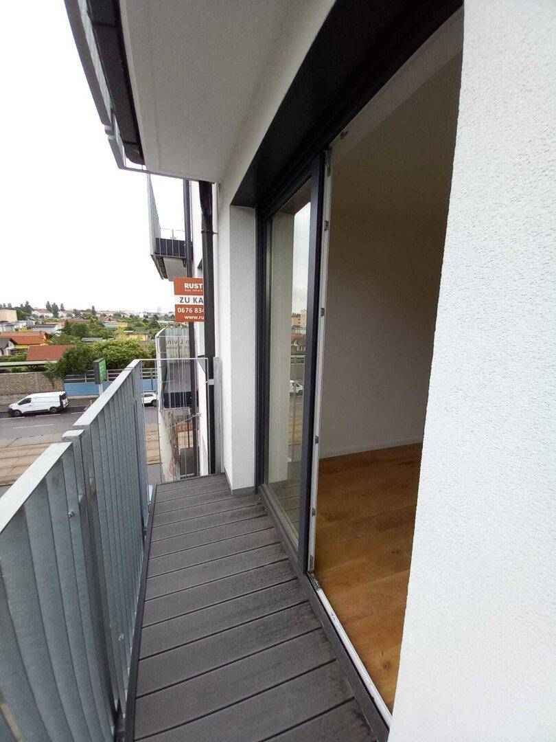 Schmaler Balkon mit grauem Bodenbelag und Blick auf die Straße sowie umliegende Gebäude.