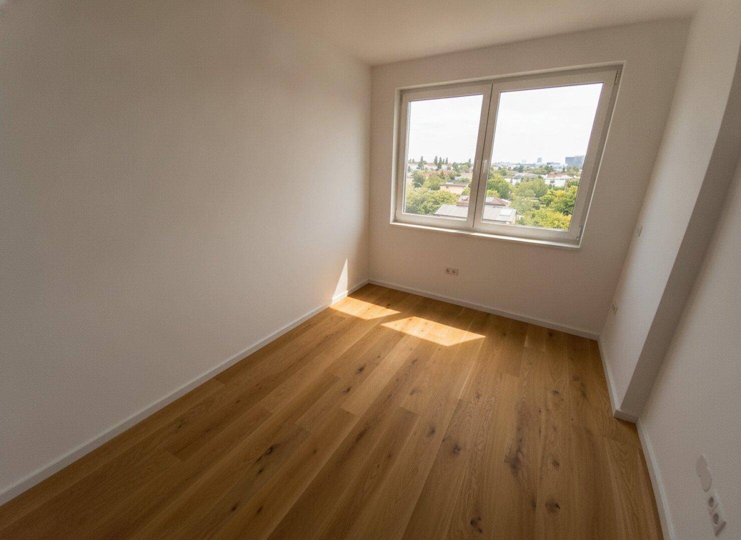 Helles Zimmer mit Holzboden und Fenster, das einen angenehmen Blick ins Grüne bietet.