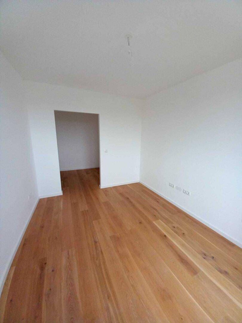 Kleineres, helles Zimmer mit Holzboden, ideal als Kinder- oder Gästezimmer in einem Neubau.