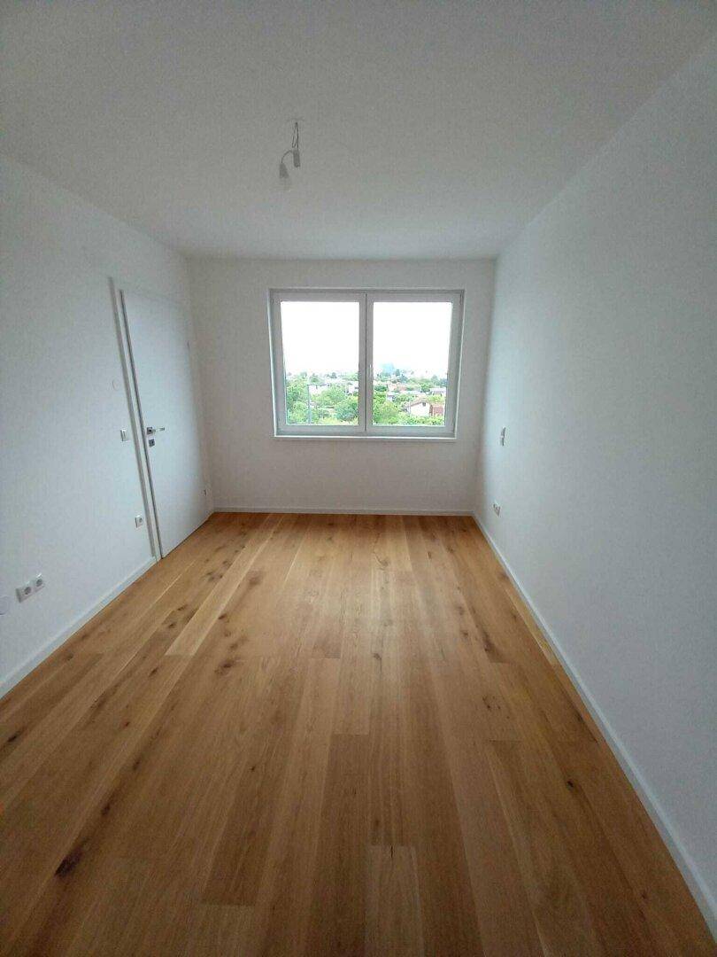 Freundliches Zimmer mit Holzboden und Fenster, ideal als Schlaf- oder Arbeitszimmer nutzbar.
