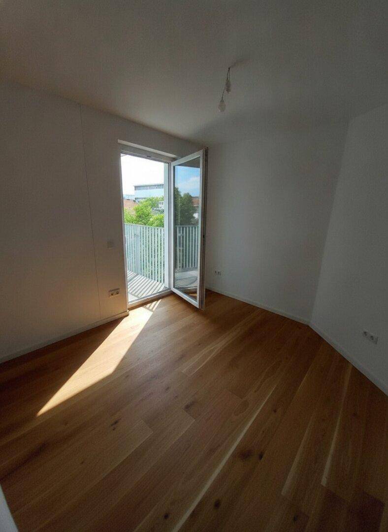 Unmöblierter Raum mit Holzboden und Balkonzugang, der von der Sonne durchflutet wird.