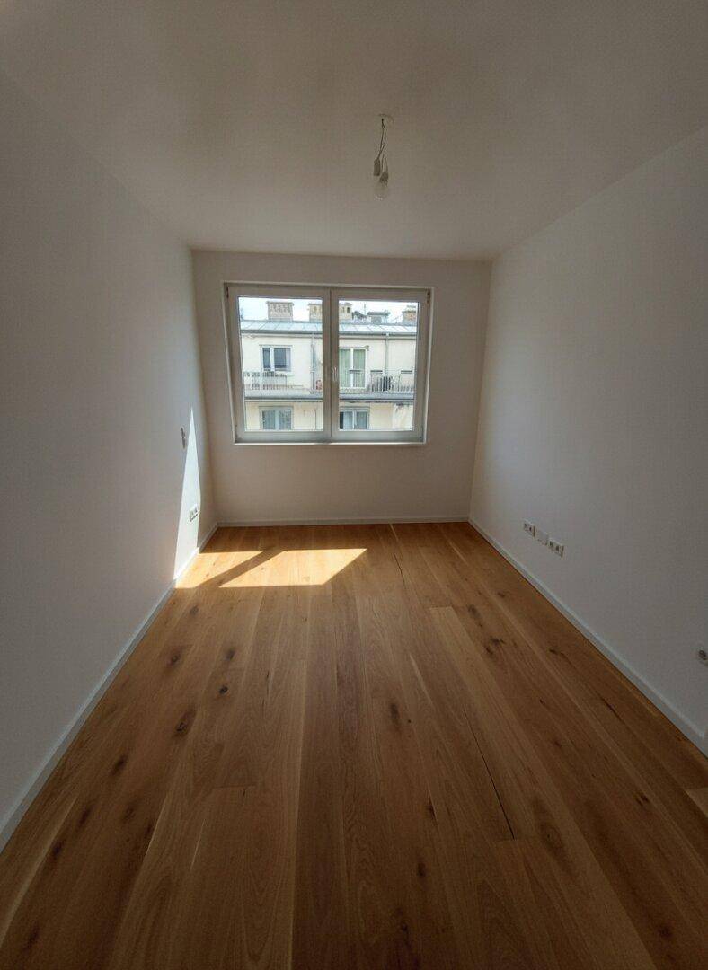 Leeres Schlafzimmer mit Holzparkettboden und Fensterblick auf die Stadt.
