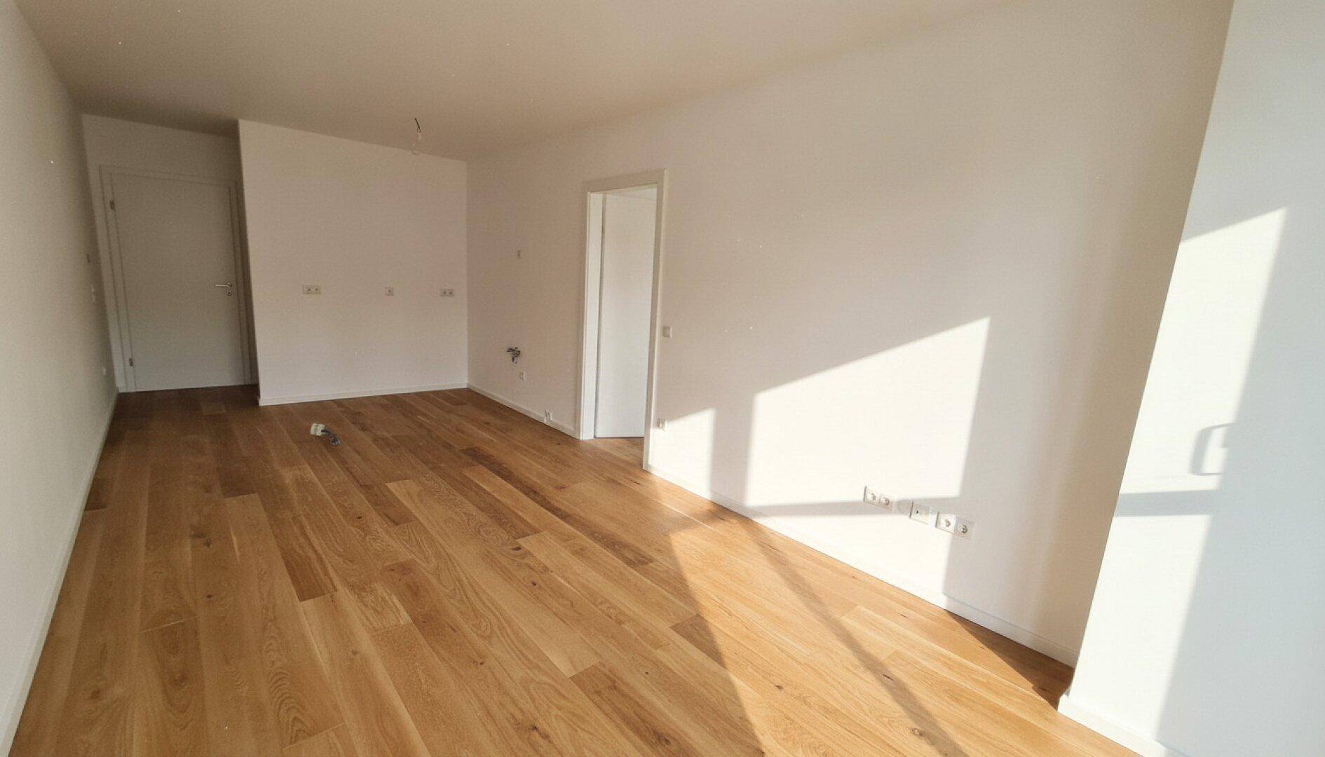Heller, leerer Wohnraum mit neuem Holzparkettboden und viel natürlichem Licht.