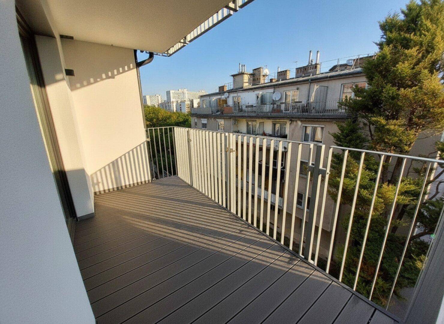 Balkon mit modernem Holzboden und Blick auf die umliegenden Gebäude und grüne Bäume.