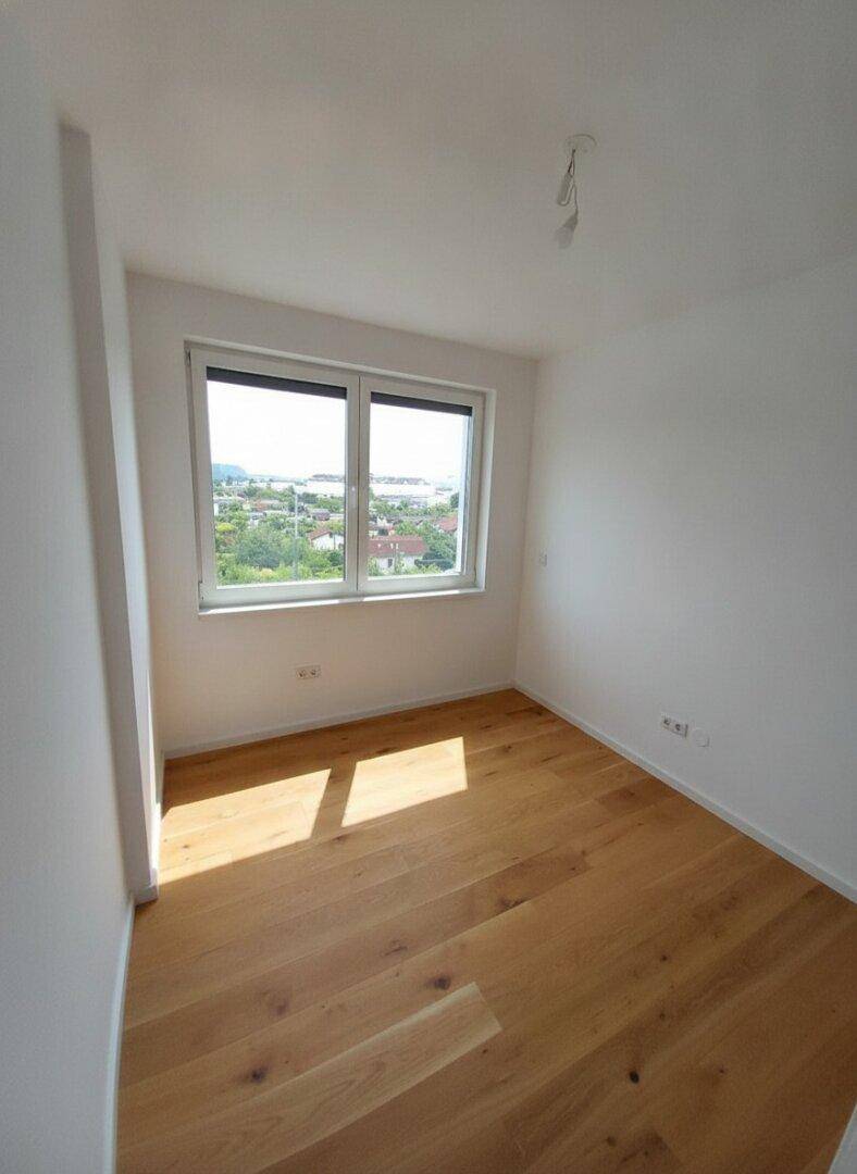 Helles Zimmer mit Holzboden und Fenster, das einen weiten Blick über die Landschaft bietet.