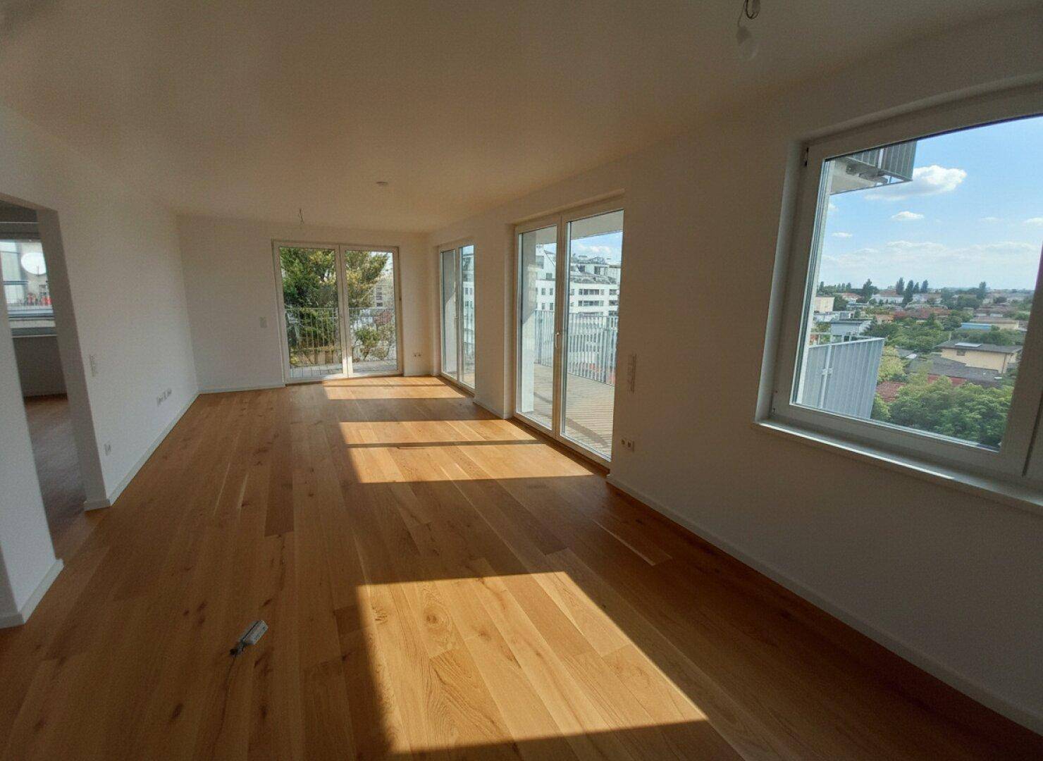 Heller Wohnraum mit Holzboden, großen Fenstern und direktem Zugang zu einem Balkon.