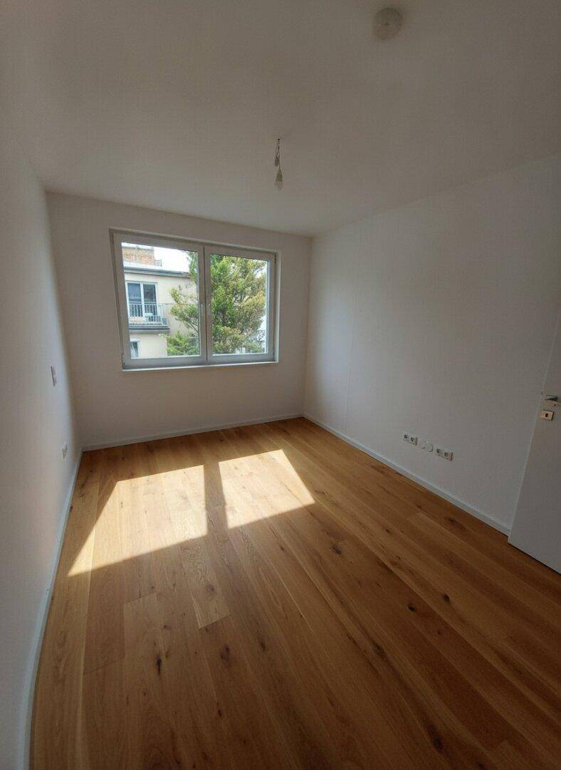 Freundliches Zimmer mit Holzboden und Fenster mit Blick ins Grüne, ideal für Ruhe und Entspannung.