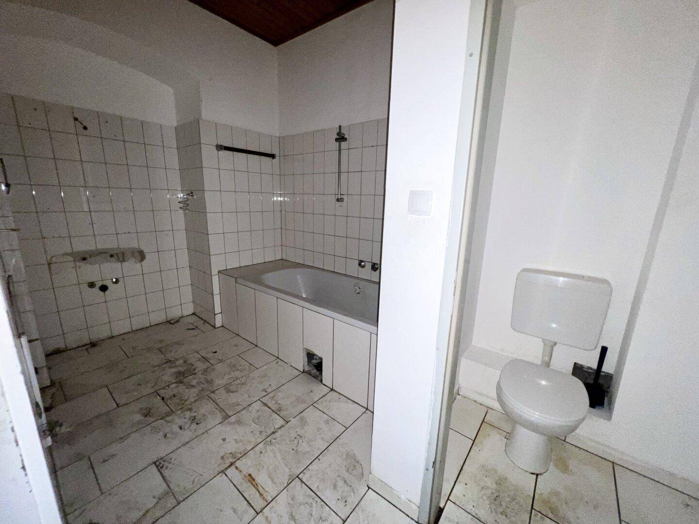 Badezimmer mit Badewanne und WC, gefliest und in renovierungsbedürftigem Zustand.