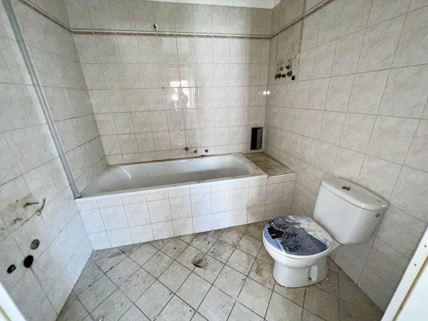 Badezimmer mit eingebauter Badewanne und Toilette, gefliesten Wänden und Boden, das Renovierung erfordert.