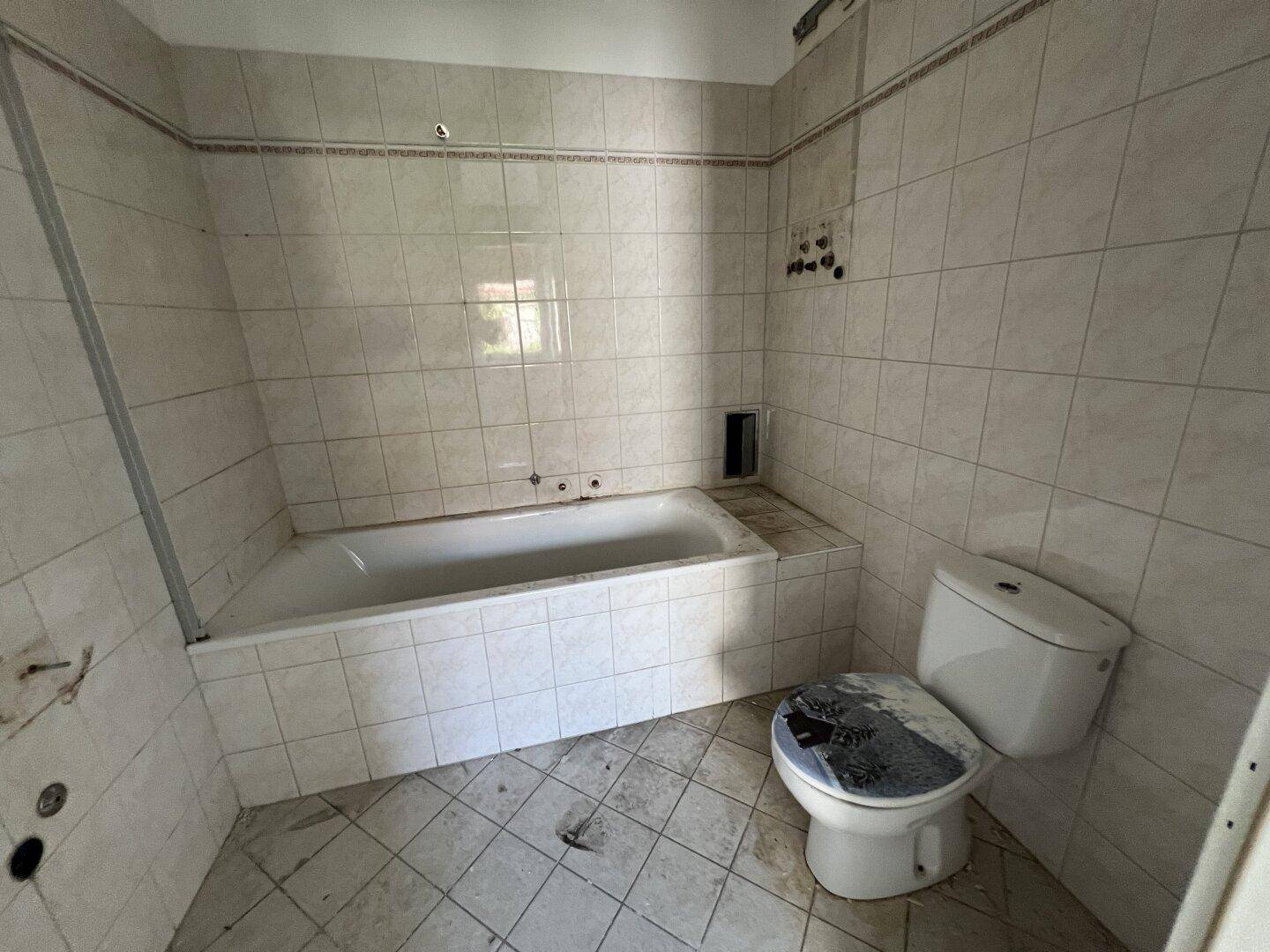Badezimmer mit Badewanne und Toilette, komplett gefliest, in einem Zustand, der eine Modernisierung benötigt.