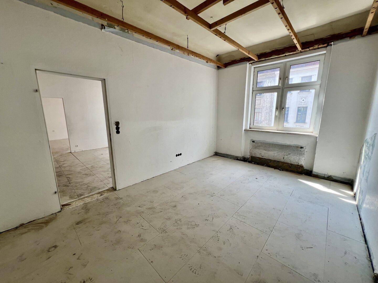 Leerer Raum mit einem Fenster und freiliegender Deckenkonstruktion, bereit für die Renovierung.