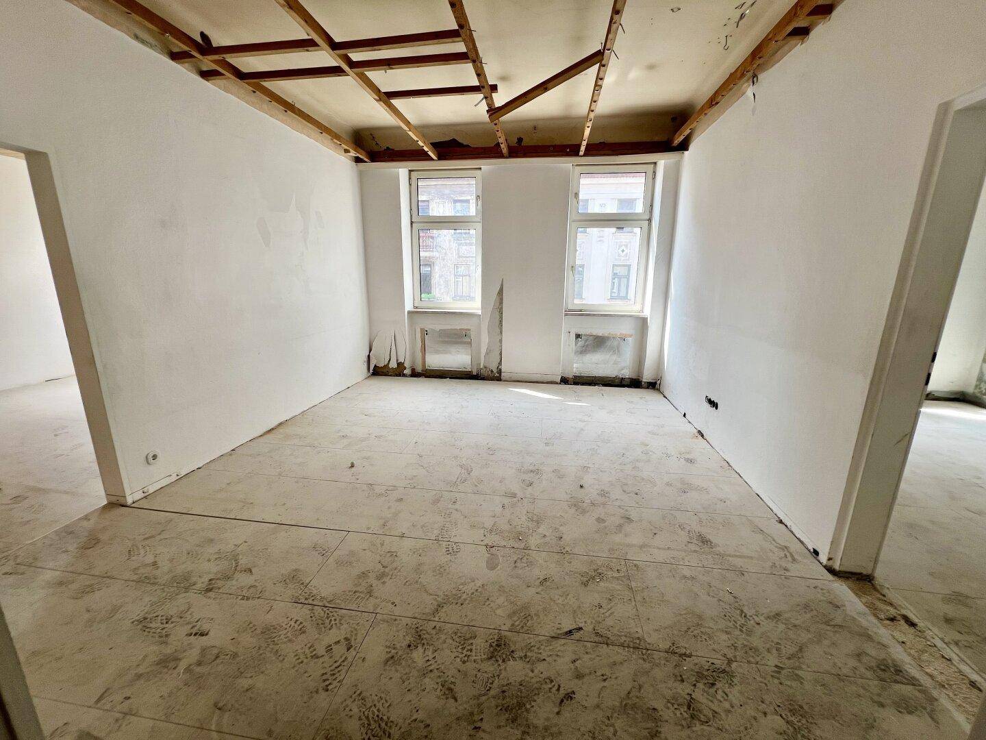 Unmöblierter Raum mit zwei Fenstern und sichtbarer Deckenunterkonstruktion, wartet auf Ausbau.