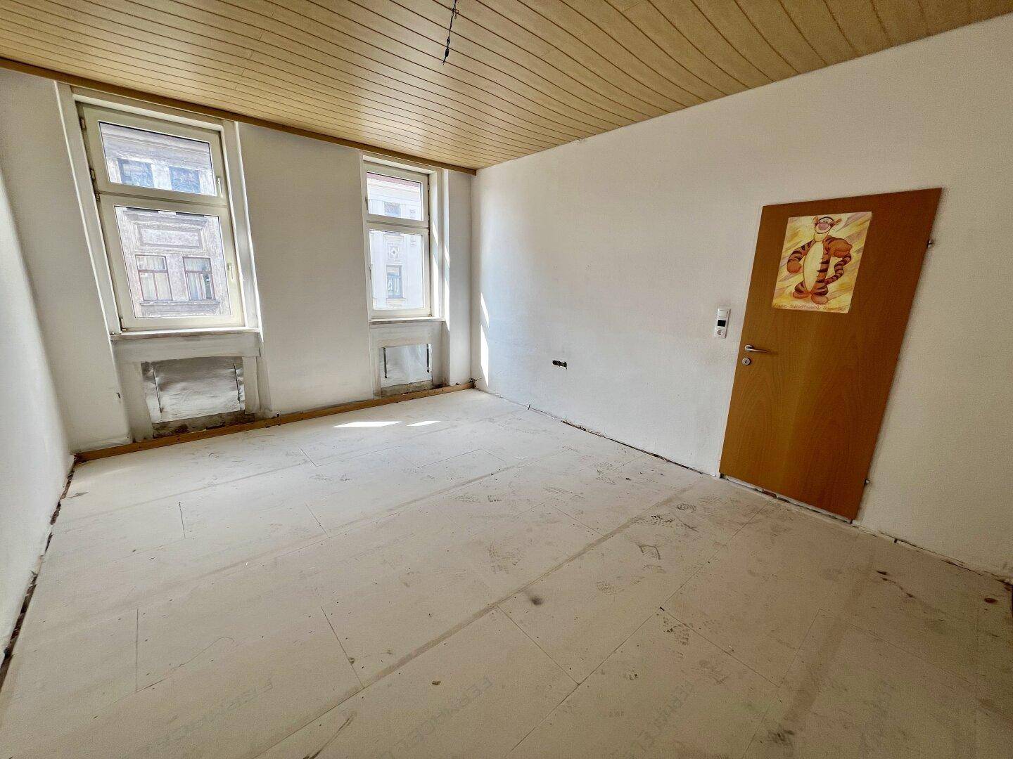 Heller, unmöblierter Raum mit Holzpaneeldecke und zwei Fenstern, bereit zur Neugestaltung.