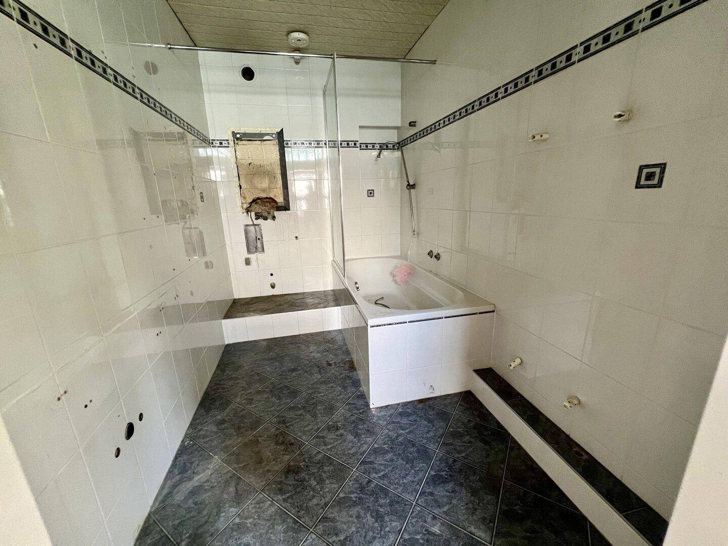 Badezimmer in Renovierung mit weiß gefliesten Wänden, dunklem Boden und einer Badewanne.