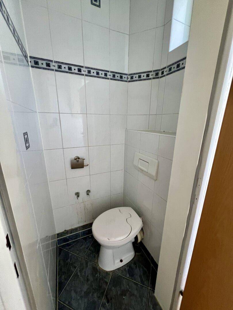 Kleines WC mit weißen Wandfliesen und dunklem Boden, in einfachem, funktionalem Zustand.