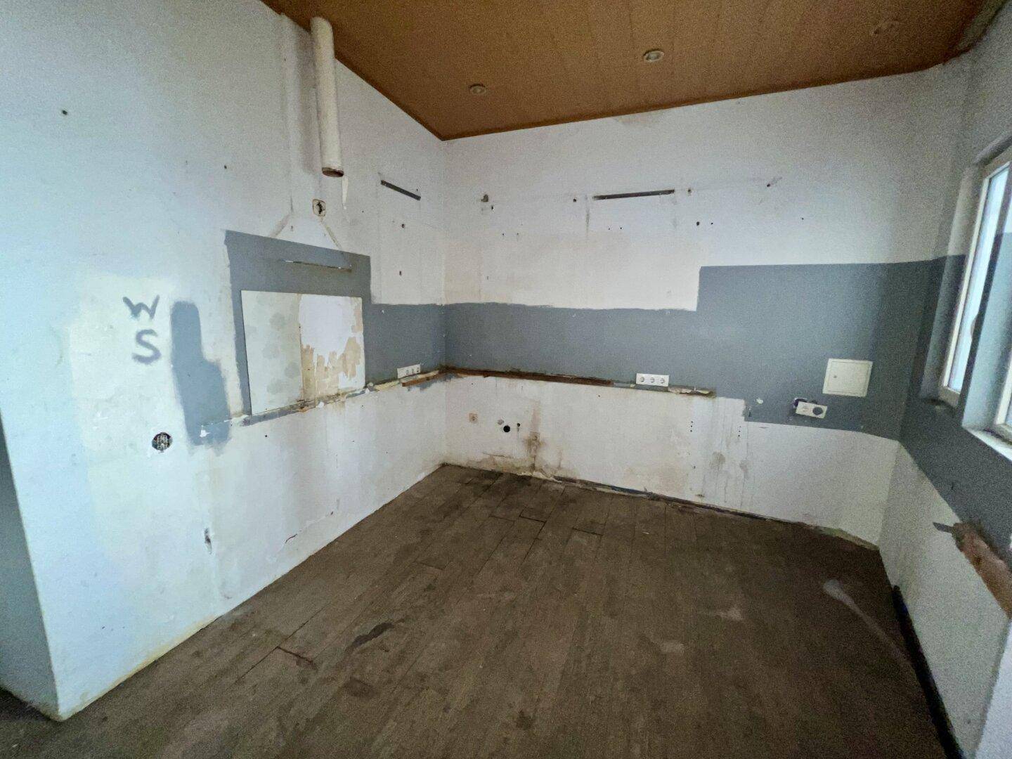Leere Küche mit Anschlüssen und Fenstern, bereit für den Einbau einer neuen Küchenzeile.