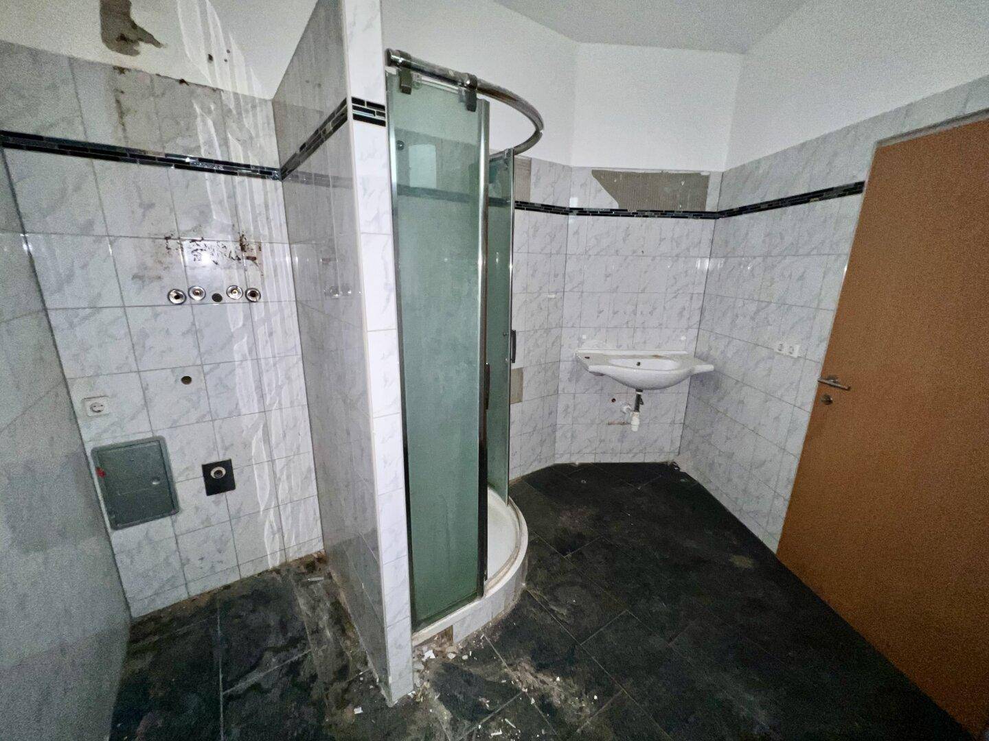 Badezimmer mit Duschkabine, Waschbecken und Fliesenboden, in renovierungsbedürftigem Zustand.