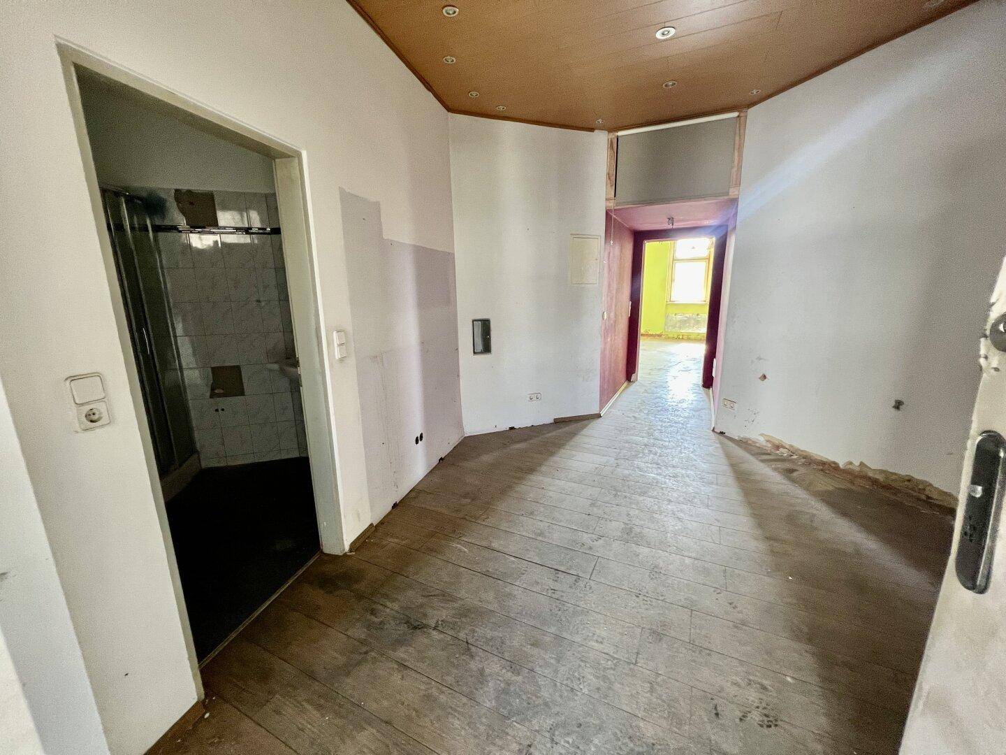 Langer Flur mit Holzboden und Zugang zu verschiedenen Räumen, renovierungsbedürftig.