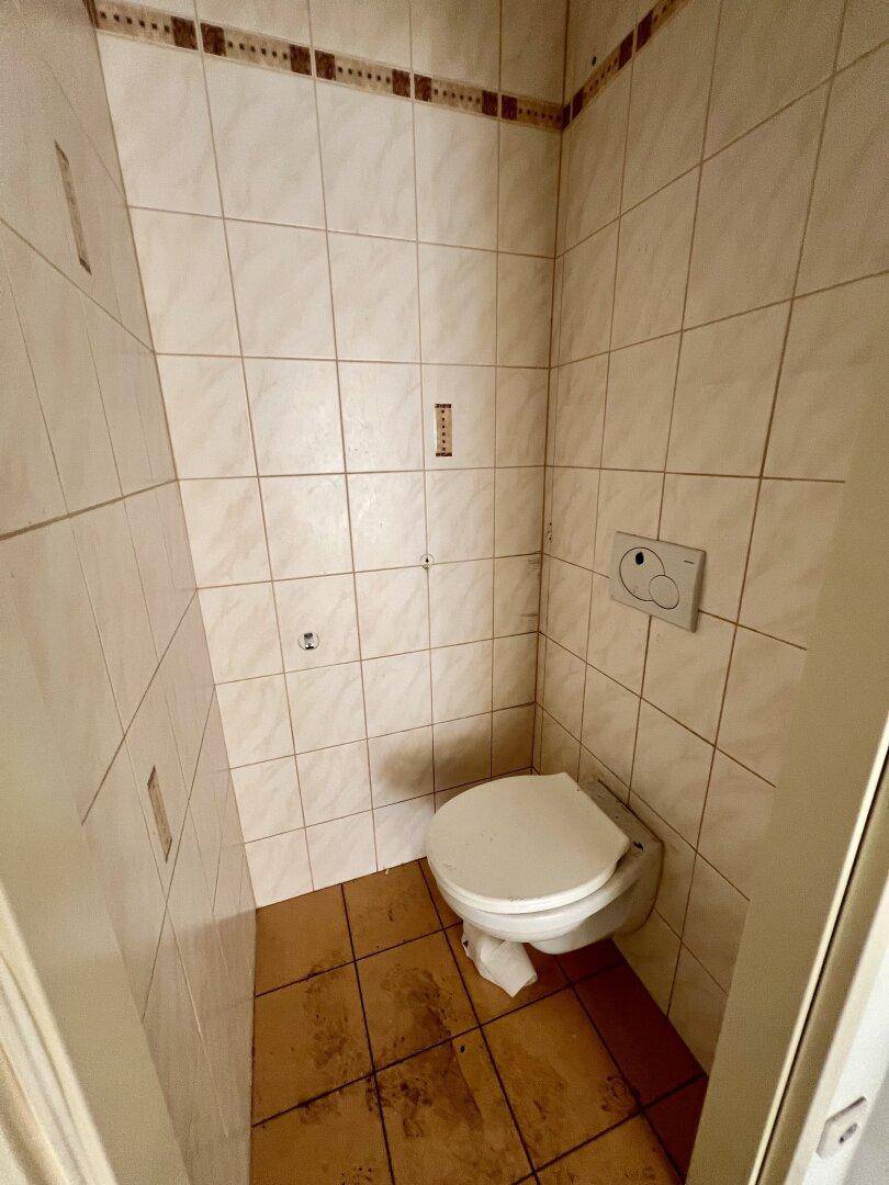 Kleines WC mit Wandtoilette und beigefarbenen Fliesen, das einfach ausgestattet ist.