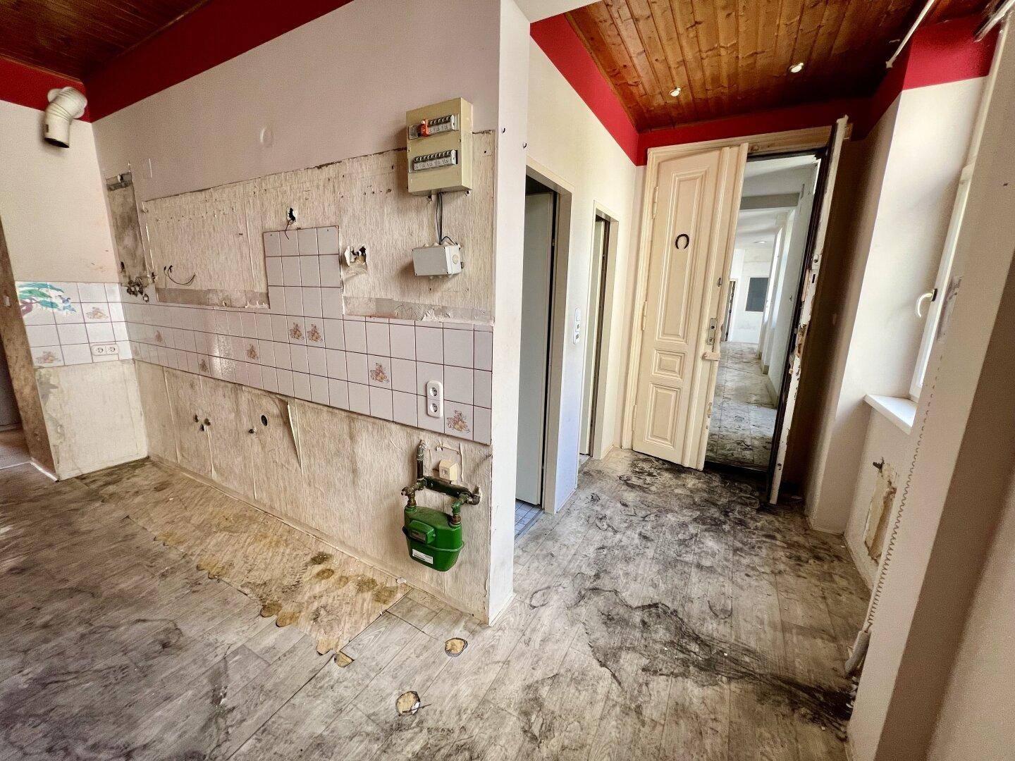 Renovierungsbedürftige Küche mit freiliegenden Wänden, Gaszähler und Zugang zu einem Flur.
