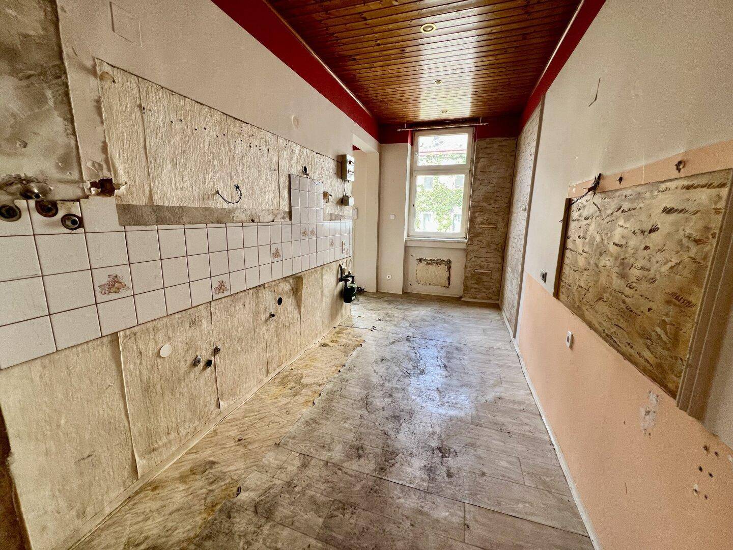 Renovierungsbedürftige Küche mit alten Fliesen, freiliegenden Wänden und Holzdecke.