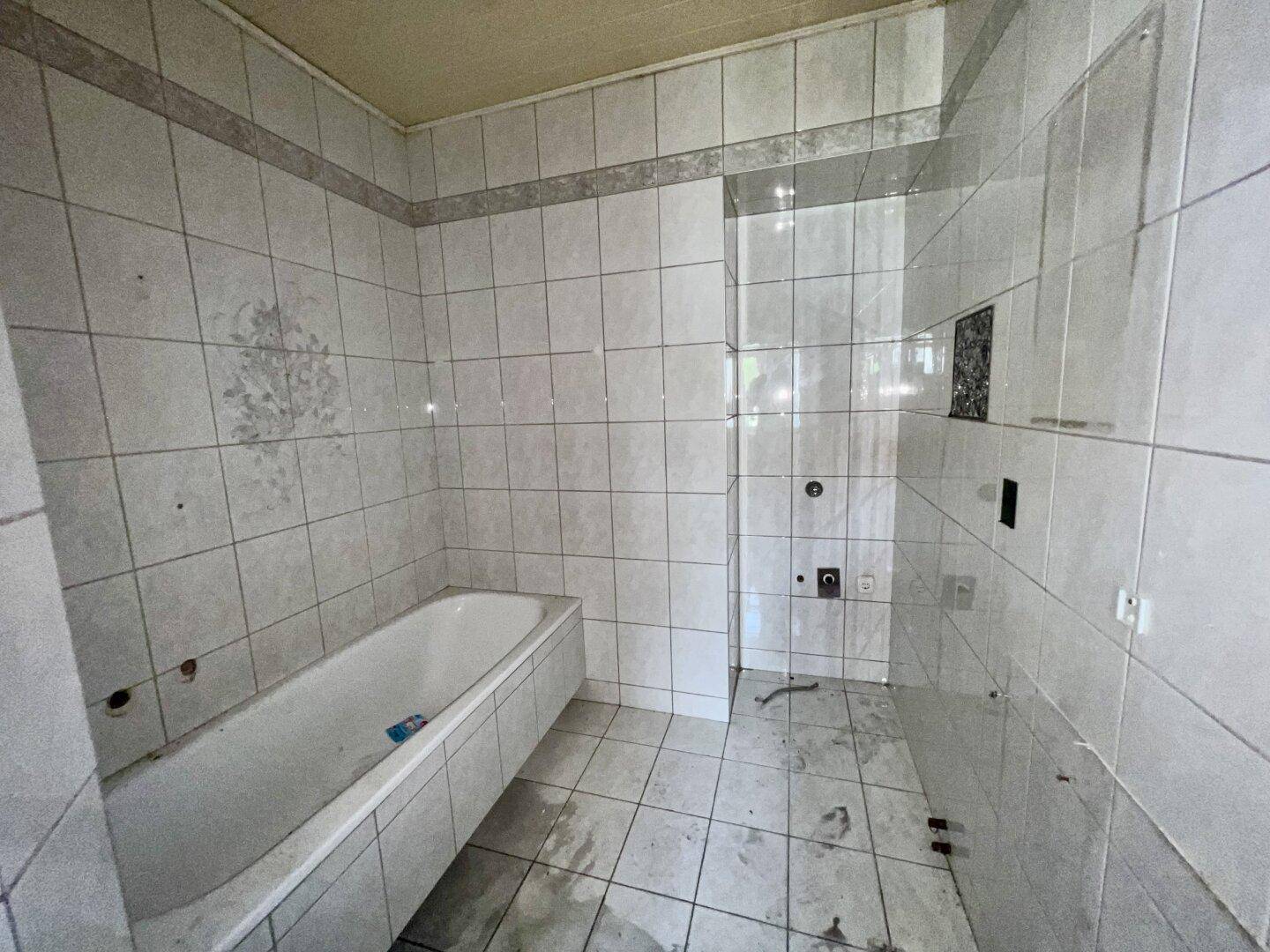 Badezimmer in Renovierung mit Fliesen, Badewanne und vorbereiteten Anschlüssen für eine Dusche.