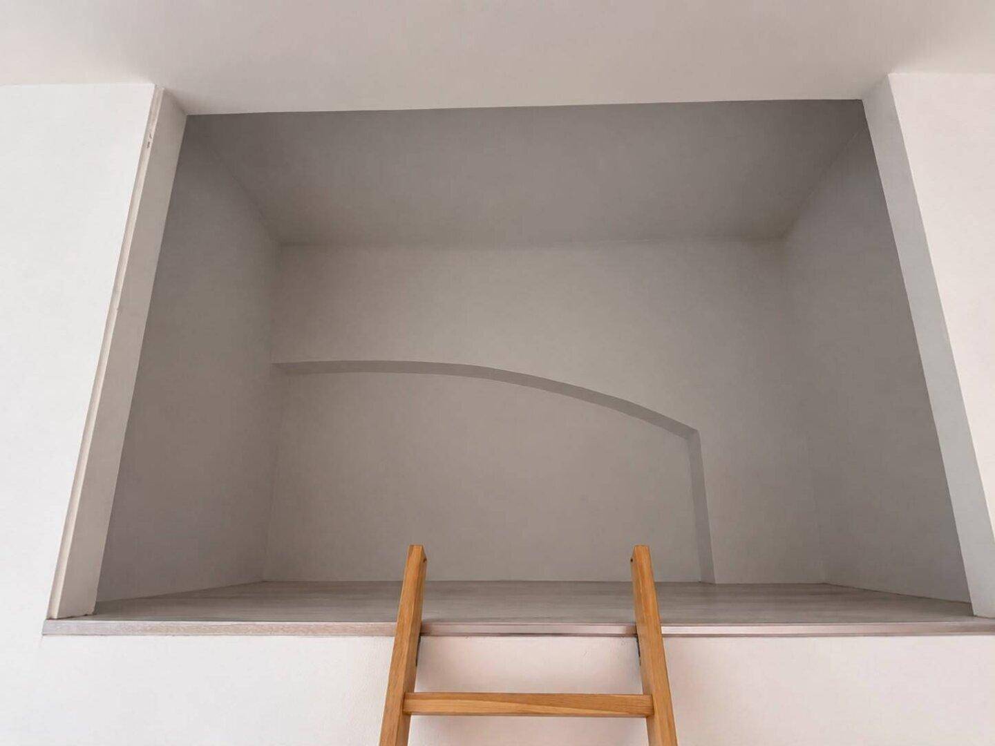 Erhöhter Schlafbereich mit Holzleiter und minimalistischem Design.