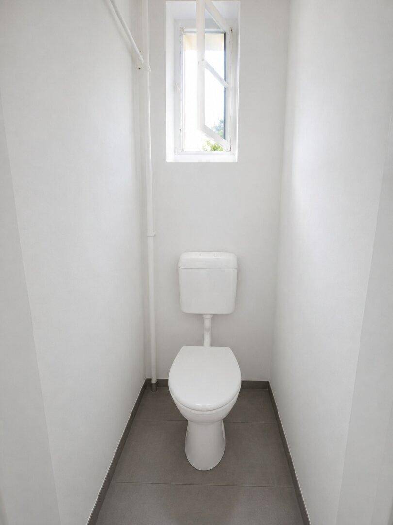 Schlichtes WC mit Fenster und Fliesenboden in einem kleinen Raum.