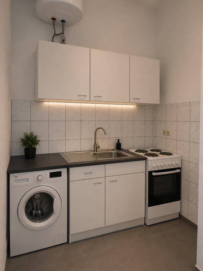 Kompakte Küchenzeile mit Waschmaschine, Spüle und Herd, ideal für kleine Wohnungen.