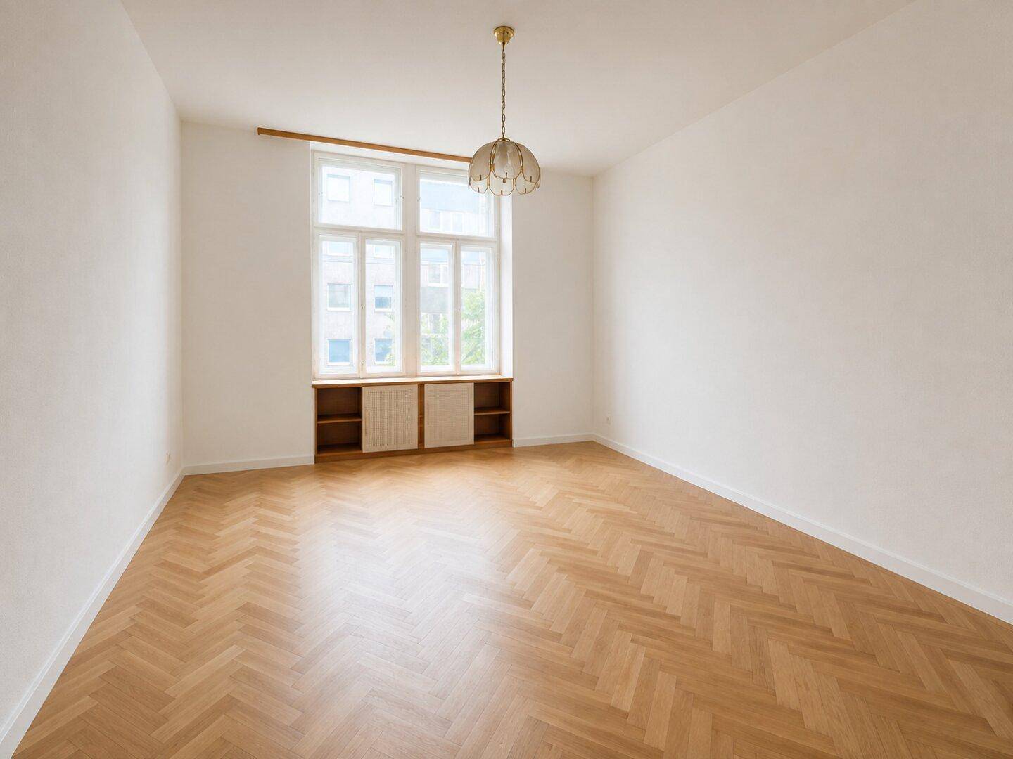 Helles, leeres Zimmer mit Fischgrätparkett und großem Fenster, bereit zur Einrichtung.