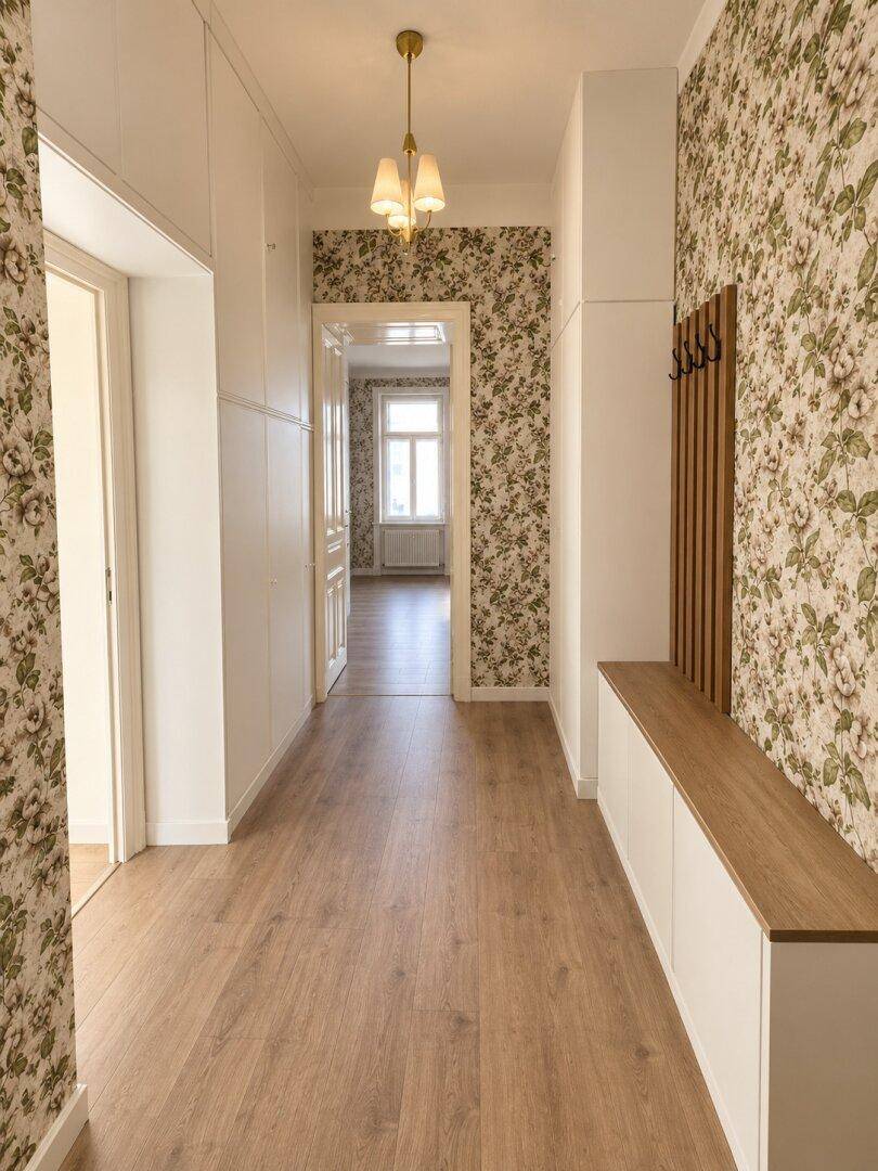 Heller Flur mit floraler Tapete, Holzfußboden und integrierter Garderobe.