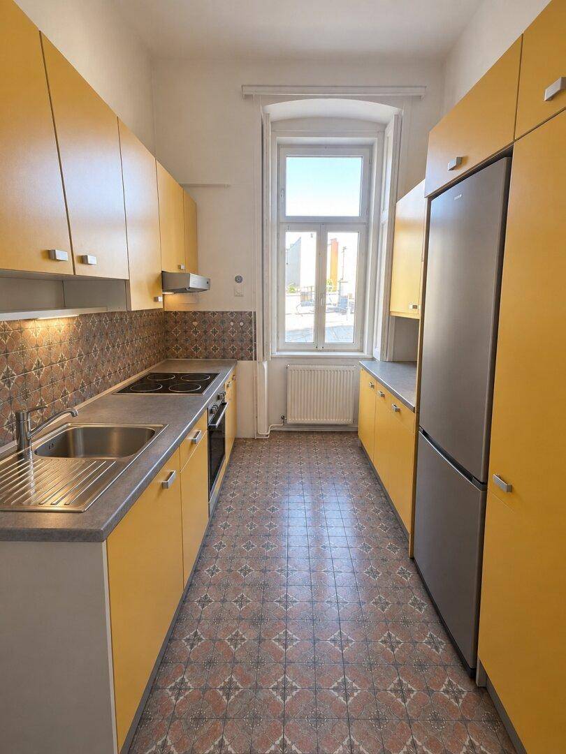 Funktionale Küche mit gelben Schränken, Fliesenboden und einem Fenster für Tageslicht.