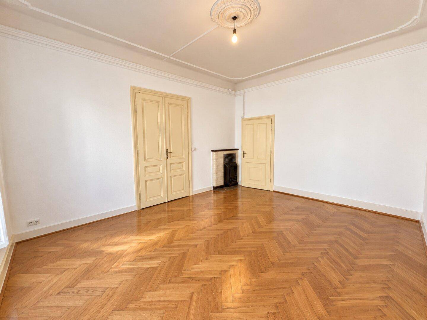 Großes Zimmer mit Fischgrätparkett, hohen Decken und einem dekorativen Kamin.